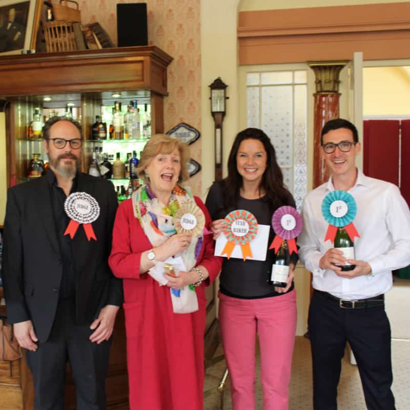 Four people standing indoors, each holding a rosette ribbon, smiling for the photo.