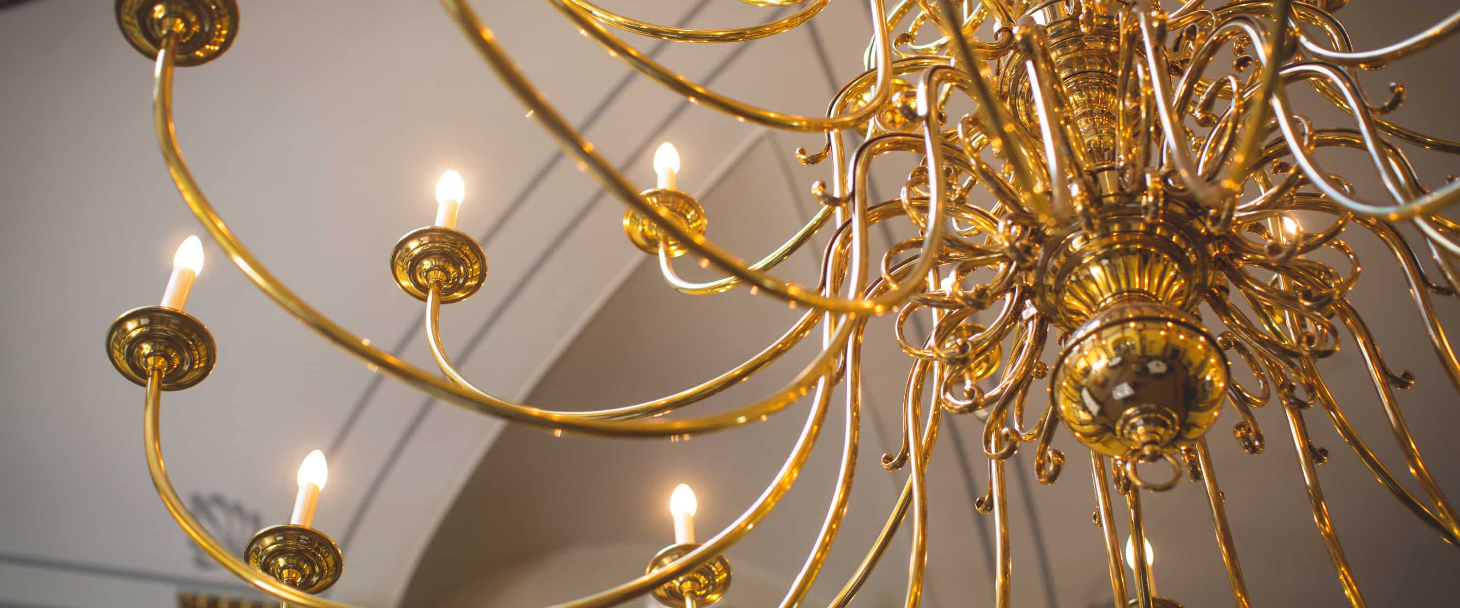 An ornate golden chandelier with lit bulbs against a soft-focus background.