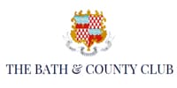 Emblem of the bath & county club featuring a shield with red and checkerboard patterns flanked by silver decorative elements.