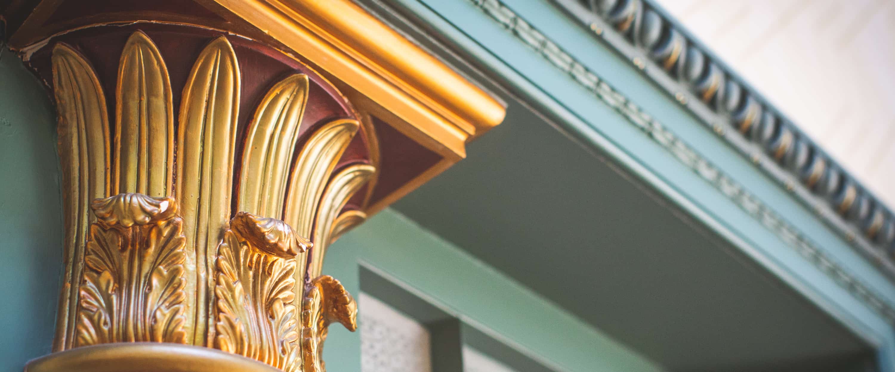 Ornate golden column capital against a soft-focus architectural background.