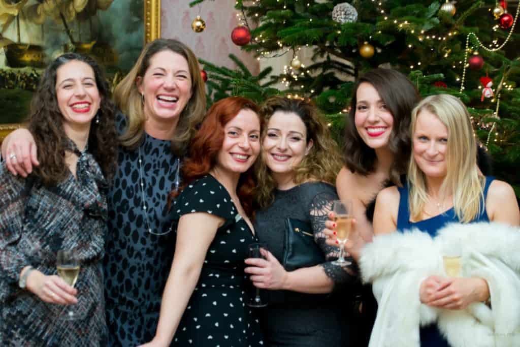 Group of women smiling together at a festive gathering with a christmas tree in the background.