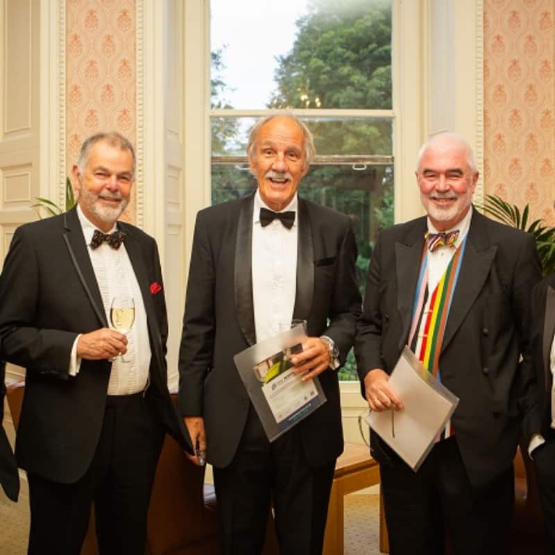 Three men in formal attire with bow ties smiling at a social event.