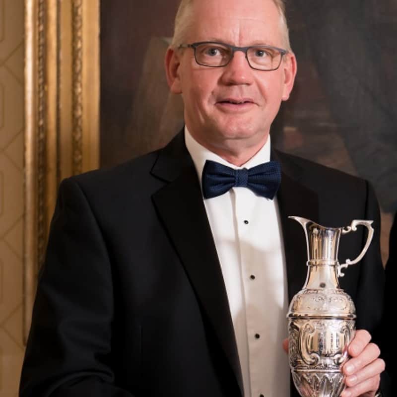 Man in tuxedo holding a silver trophy.